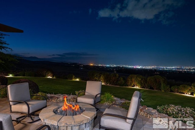 patio terrace at night featuring an outdoor fire pit and a lawn