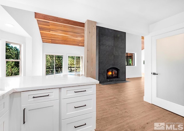 kitchen featuring light stone counters, light hardwood / wood-style flooring, a fireplace, white cabinetry, and wood ceiling