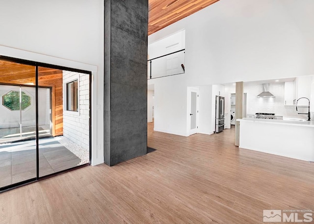 unfurnished living room with a towering ceiling, sink, and light hardwood / wood-style floors