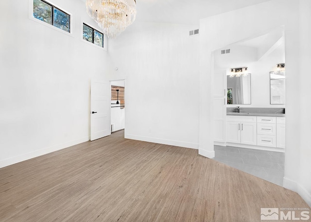 unfurnished living room with tile flooring, an inviting chandelier, a towering ceiling, and sink