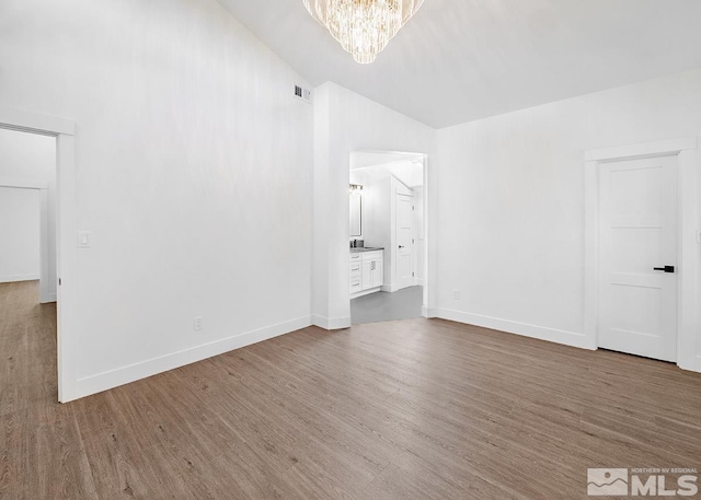 unfurnished bedroom with ensuite bathroom, vaulted ceiling, hardwood / wood-style flooring, and a chandelier