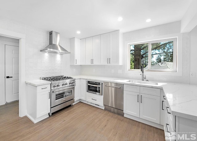 kitchen featuring wall chimney range hood, white cabinetry, light hardwood / wood-style flooring, and appliances with stainless steel finishes