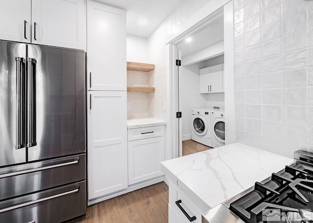 kitchen featuring washing machine and dryer, high end fridge, tasteful backsplash, and light wood-type flooring