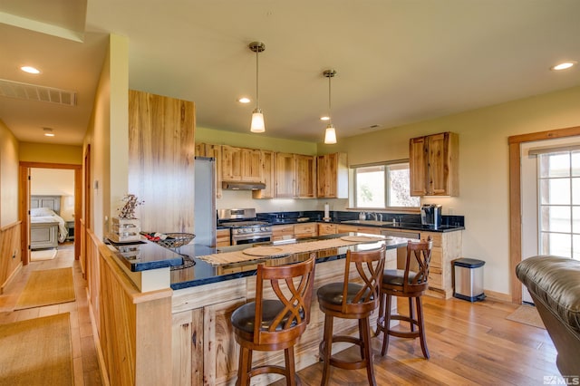 kitchen featuring appliances with stainless steel finishes, kitchen peninsula, light wood-type flooring, hanging light fixtures, and a kitchen breakfast bar