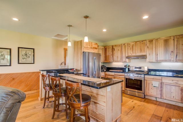 kitchen with hanging light fixtures, appliances with stainless steel finishes, a kitchen bar, light hardwood / wood-style flooring, and a center island