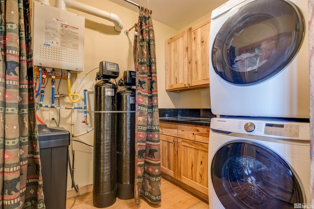 laundry area with light hardwood / wood-style floors, cabinets, stacked washer / drying machine, and water heater