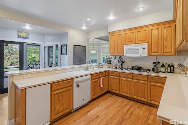 kitchen with pendant lighting, kitchen peninsula, white appliances, light wood-type flooring, and sink