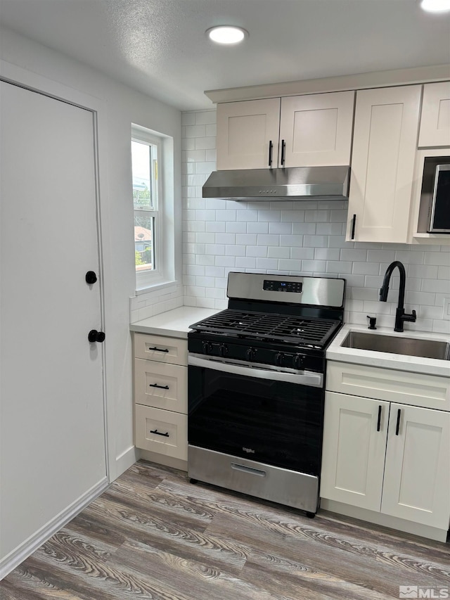 kitchen with gas range, backsplash, light hardwood / wood-style floors, sink, and white cabinets