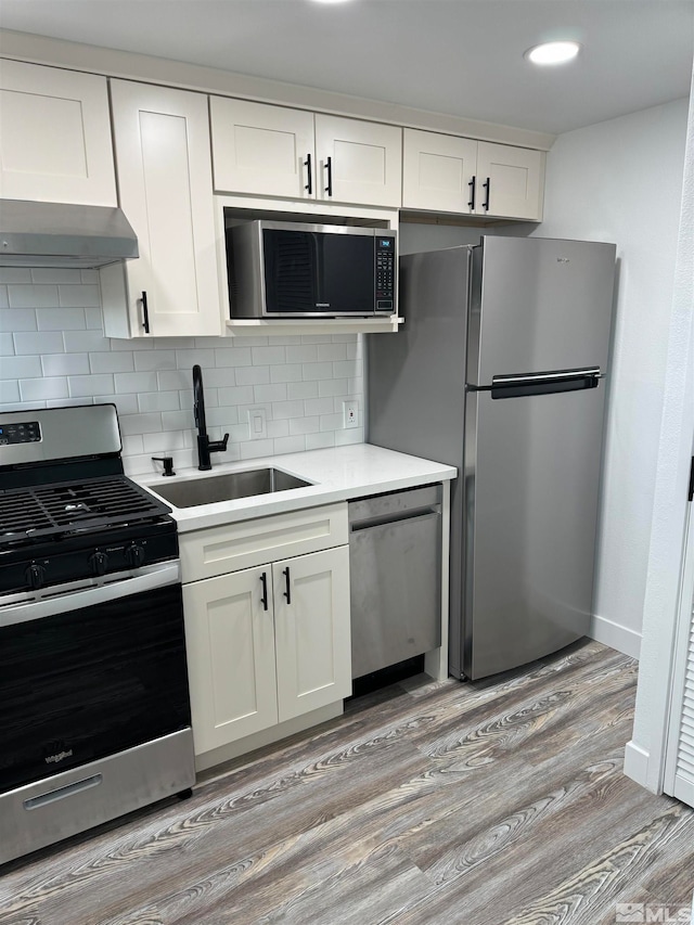 kitchen with wall chimney range hood, light hardwood / wood-style flooring, appliances with stainless steel finishes, white cabinets, and backsplash