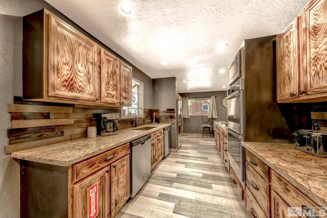 kitchen featuring sink, light stone counters, appliances with stainless steel finishes, light hardwood / wood-style flooring, and a textured ceiling