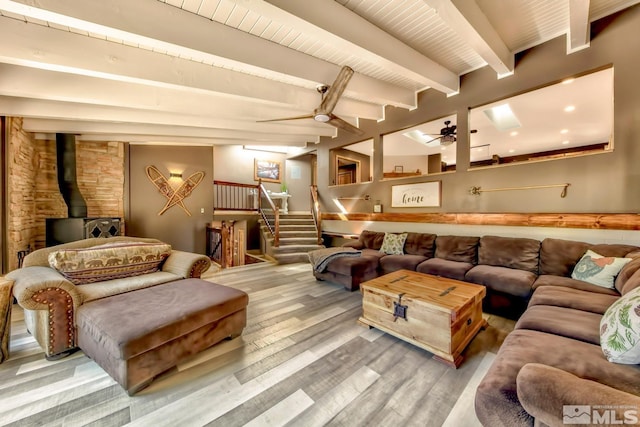 living room featuring beam ceiling, ceiling fan, a wood stove, and light wood-type flooring