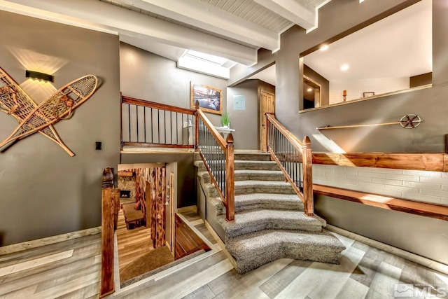 stairway featuring a skylight, light hardwood / wood-style floors, and beam ceiling