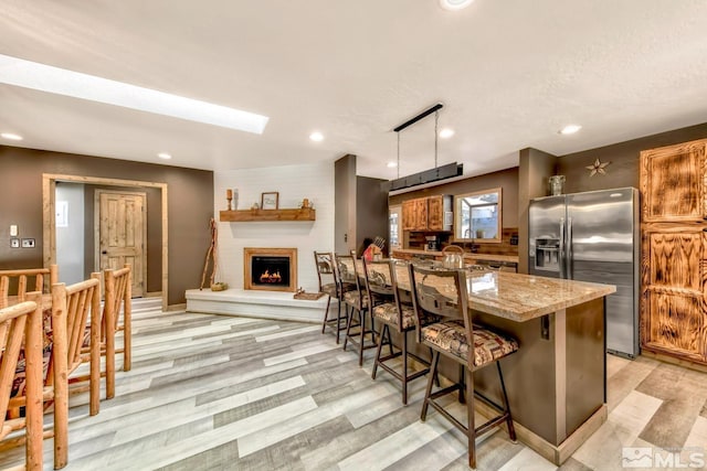 kitchen featuring a breakfast bar, stainless steel fridge, light wood-type flooring, and a fireplace