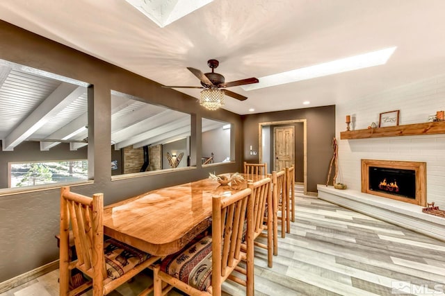 dining room featuring light hardwood / wood-style floors, a skylight, ceiling fan, a fireplace, and beam ceiling