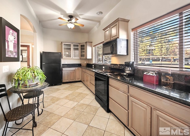 kitchen with light brown cabinets, light tile floors, ceiling fan, black appliances, and dark stone countertops