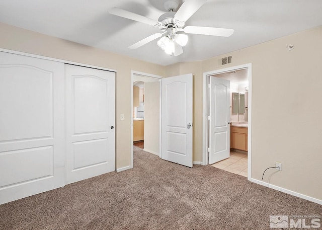 unfurnished bedroom with a closet, ensuite bath, ceiling fan, and light colored carpet