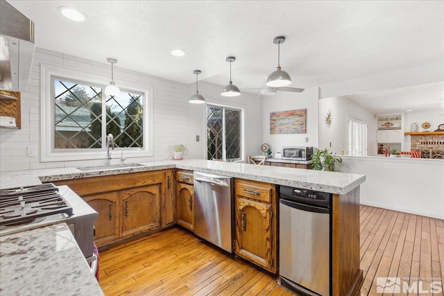 kitchen with stainless steel dishwasher, kitchen peninsula, light hardwood / wood-style flooring, pendant lighting, and sink