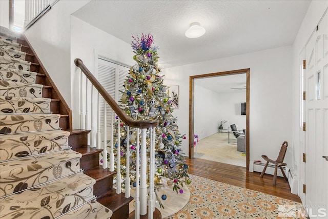 stairway with light hardwood / wood-style floors, a textured ceiling, and a baseboard heating unit