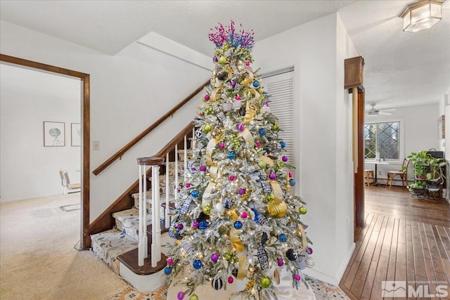 staircase with light carpet, ceiling fan, and a textured ceiling