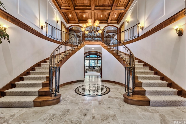 staircase featuring coffered ceiling, an inviting chandelier, light tile flooring, and a high ceiling