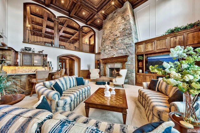 living room featuring beamed ceiling, coffered ceiling, a towering ceiling, a stone fireplace, and light carpet