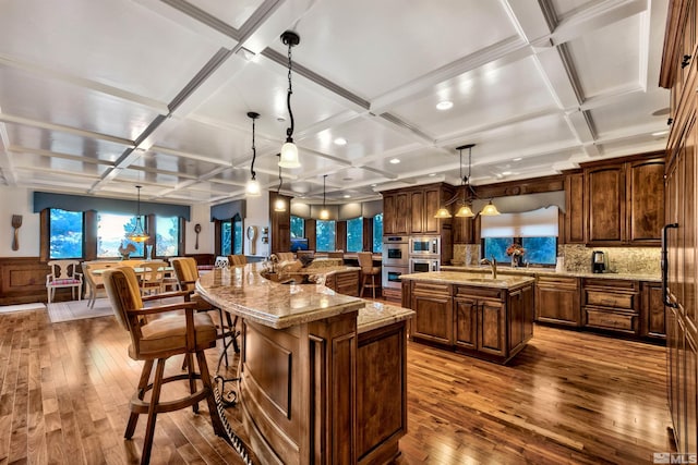 kitchen featuring coffered ceiling, a spacious island, a breakfast bar area, pendant lighting, and wood-type flooring