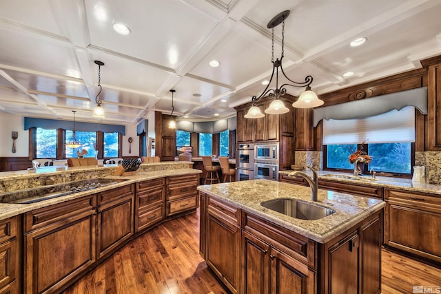 kitchen featuring coffered ceiling, sink, tasteful backsplash, and a kitchen island with sink