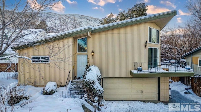 snow covered house with a deck with mountain view and a garage