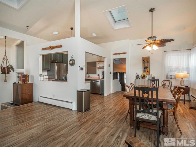 dining area featuring ceiling fan, vaulted ceiling with skylight, sink, baseboard heating, and dark hardwood / wood-style flooring