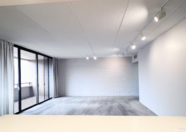 carpeted spare room with brick wall, floor to ceiling windows, and a textured ceiling