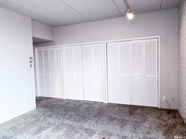 unfurnished bedroom with rail lighting, two closets, and carpet flooring