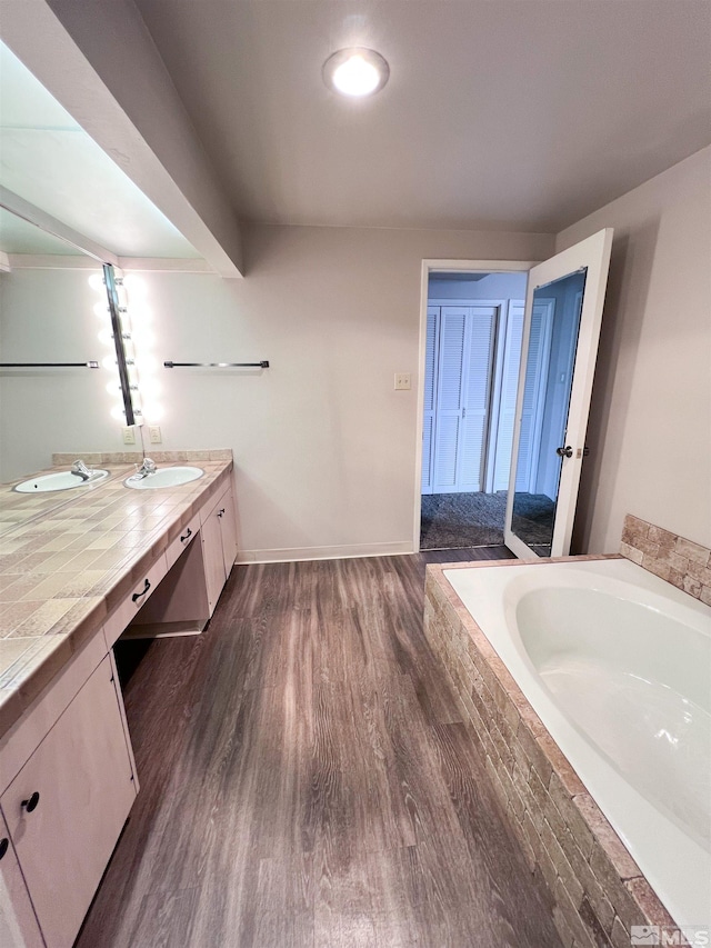 bathroom featuring hardwood / wood-style flooring, a relaxing tiled tub, and vanity