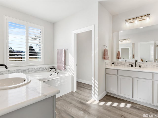 bathroom with a bath, hardwood / wood-style floors, tasteful backsplash, and vanity with extensive cabinet space