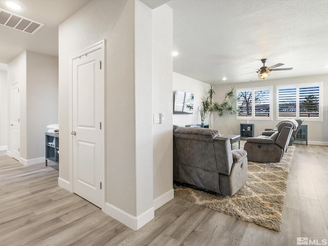 living room with a textured ceiling, ceiling fan, and light wood-type flooring