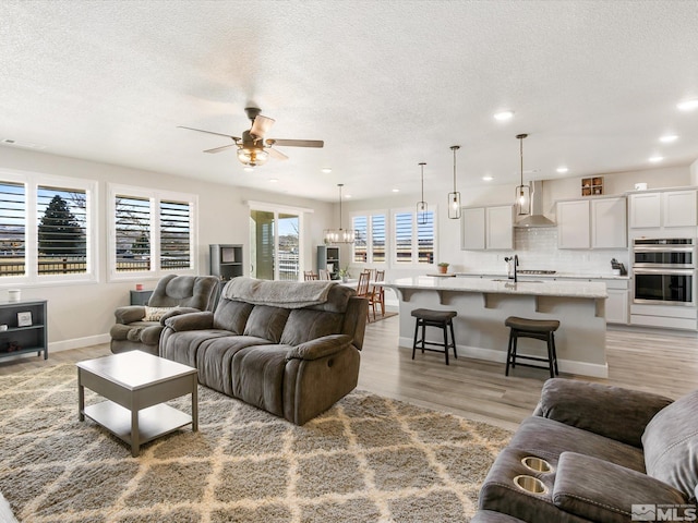 living room featuring sink, light hardwood / wood-style flooring, a textured ceiling, and ceiling fan with notable chandelier