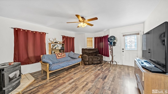 living area with ceiling fan, a wood stove, and hardwood / wood-style floors