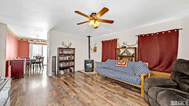 living room with a wood stove, wood-type flooring, and ceiling fan with notable chandelier