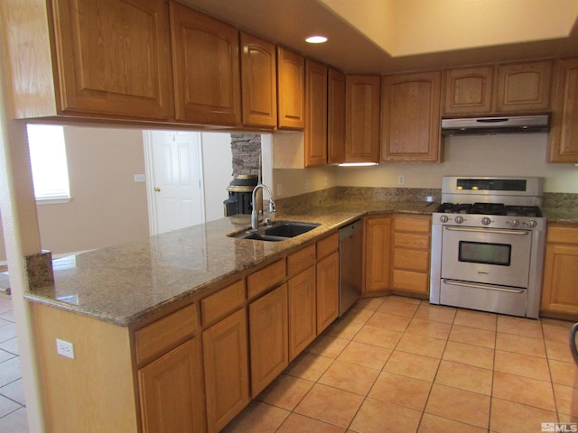 kitchen featuring light tile floors, dark stone counters, gas range oven, dishwasher, and sink