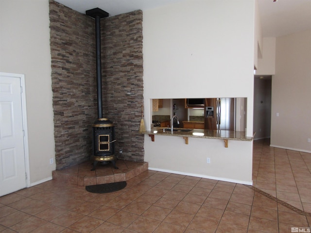 unfurnished living room featuring a high ceiling, dark tile flooring, a wood stove, and sink