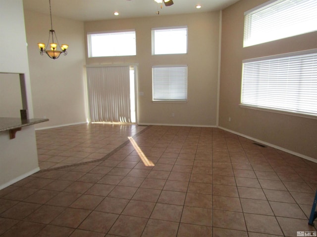 unfurnished living room with a wealth of natural light, ceiling fan with notable chandelier, a high ceiling, and dark tile flooring