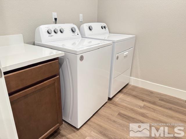 clothes washing area with cabinets, washing machine and dryer, and light hardwood / wood-style flooring