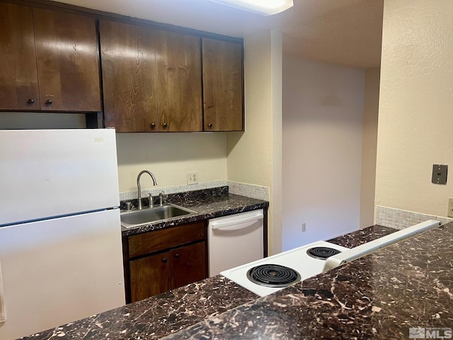 kitchen featuring dark stone countertops, dark brown cabinetry, sink, and white appliances