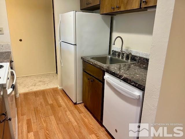 kitchen with dark stone countertops, sink, light wood-type flooring, and white appliances