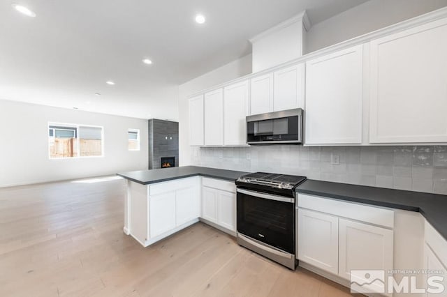 kitchen featuring stainless steel appliances, decorative backsplash, light wood-type flooring, and white cabinetry