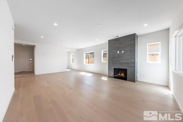 unfurnished living room with a tiled fireplace and light hardwood / wood-style flooring