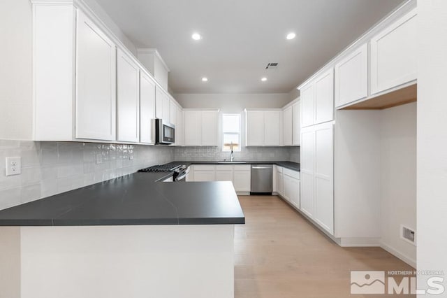 kitchen with backsplash, stainless steel appliances, sink, light wood-type flooring, and kitchen peninsula