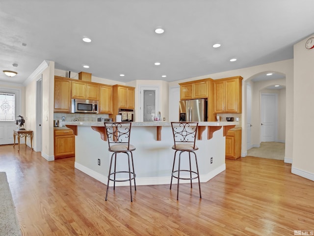 kitchen with a kitchen island, appliances with stainless steel finishes, tasteful backsplash, a kitchen breakfast bar, and light hardwood / wood-style floors