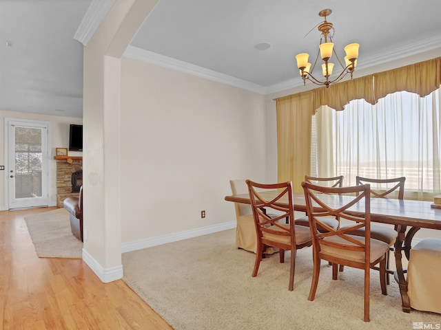 dining space featuring a fireplace, ornamental molding, a chandelier, and light wood-type flooring