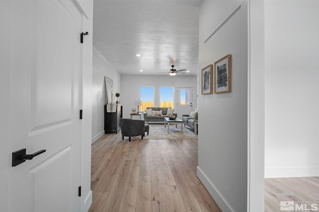 corridor with a textured ceiling and light hardwood / wood-style flooring