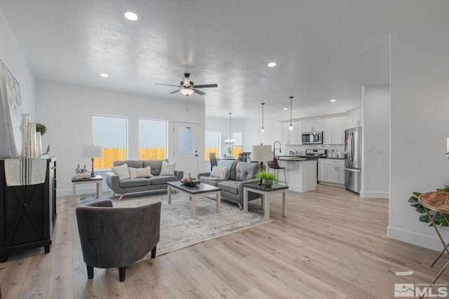 living room featuring a textured ceiling, ceiling fan with notable chandelier, and light hardwood / wood-style floors